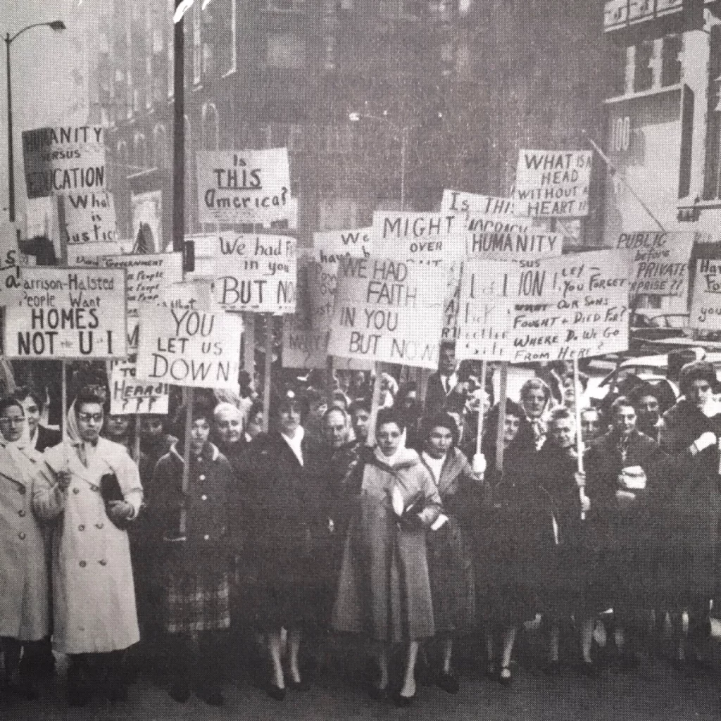 The image displays mostly women holding up signs in protest of the building of UIC. The signs are referring to Mayor Daley as he failed to serve the community.